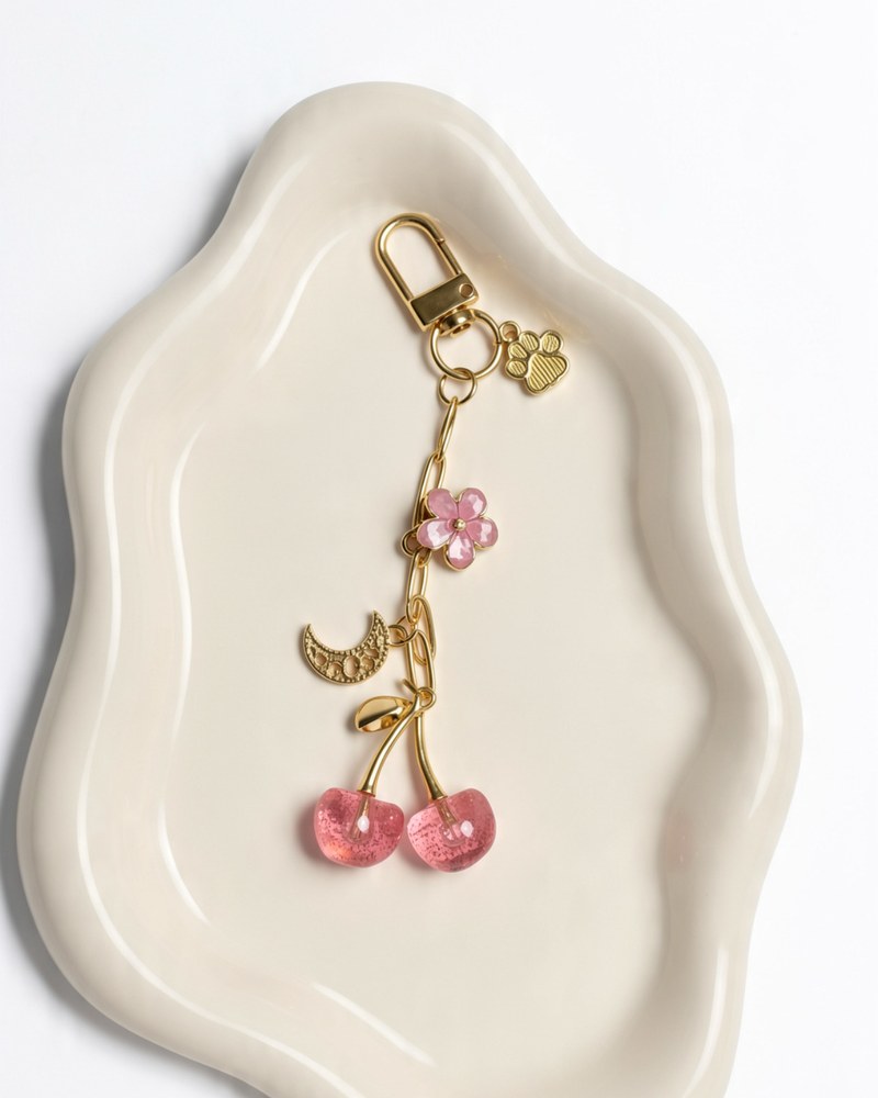 Gold chain bag charm with glittery pink cherries, a pink flower, a gold moon and a paw print charm