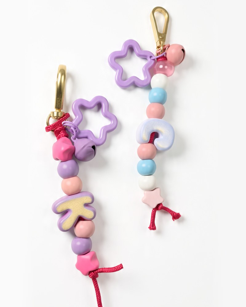 Two single initial keychains, K and C, side by side with pastel beads, bells and purple flower rings