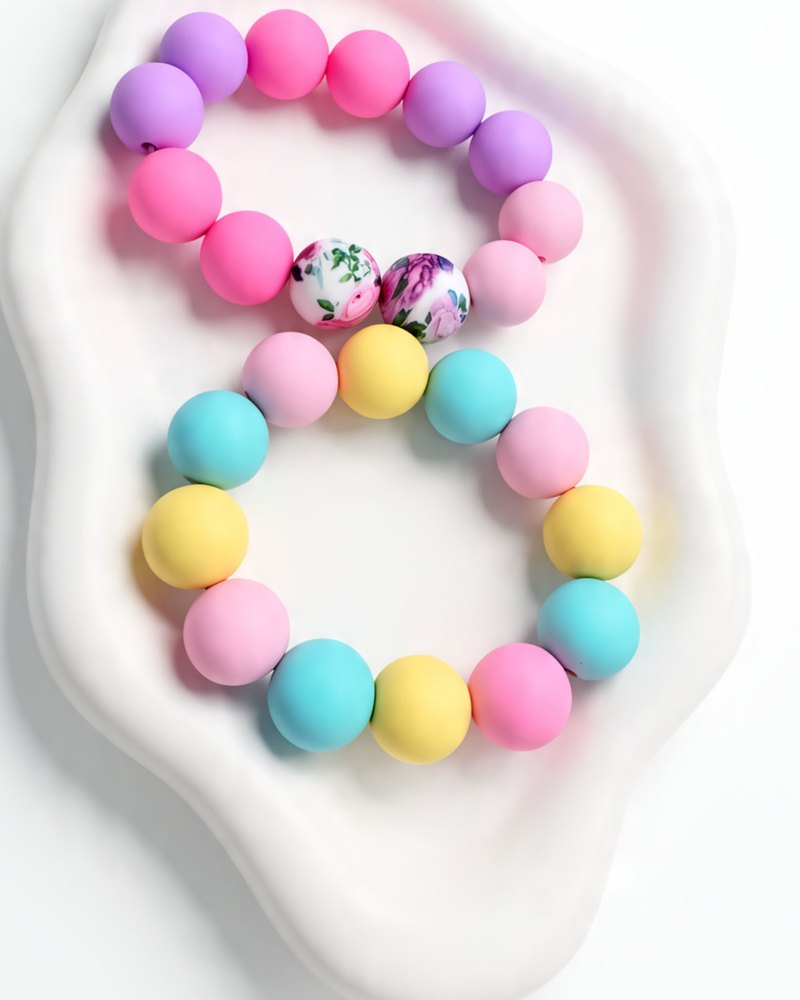 Two silicone bracelets, one lavender and pink with floral beads, one pastel rainbow