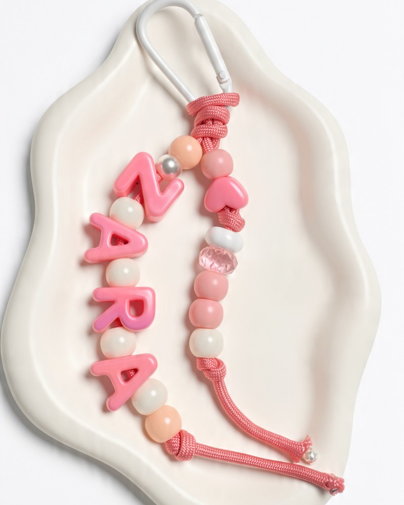 Pink double-string paracord keychain spelling ZARA with white beads between each letter, a pink heart bead and a white clip
